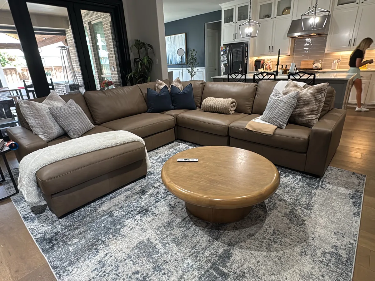 Clean open plan living room with a leather sectional and area rug after a house cleaning