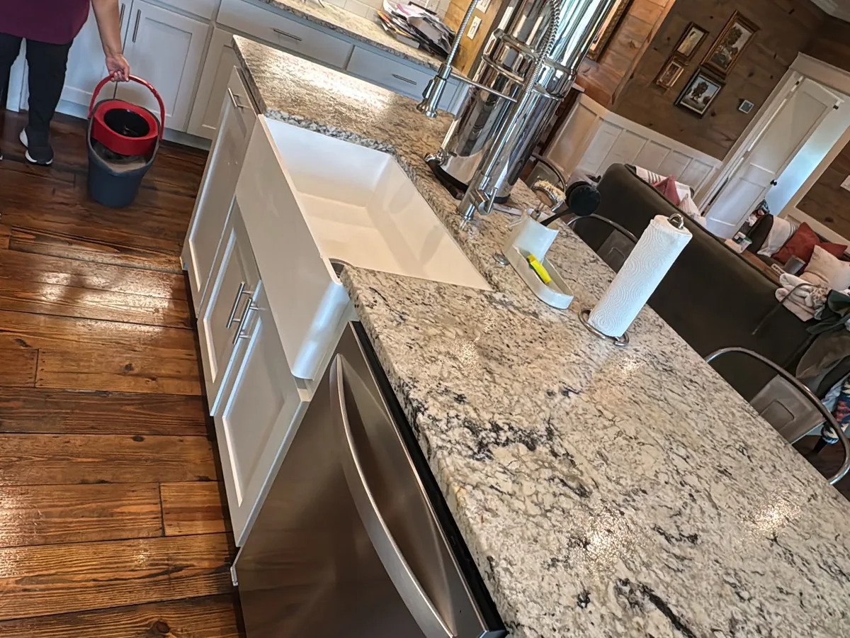 Cleared kitchen with the hardwood floor being mopped beside a granite island